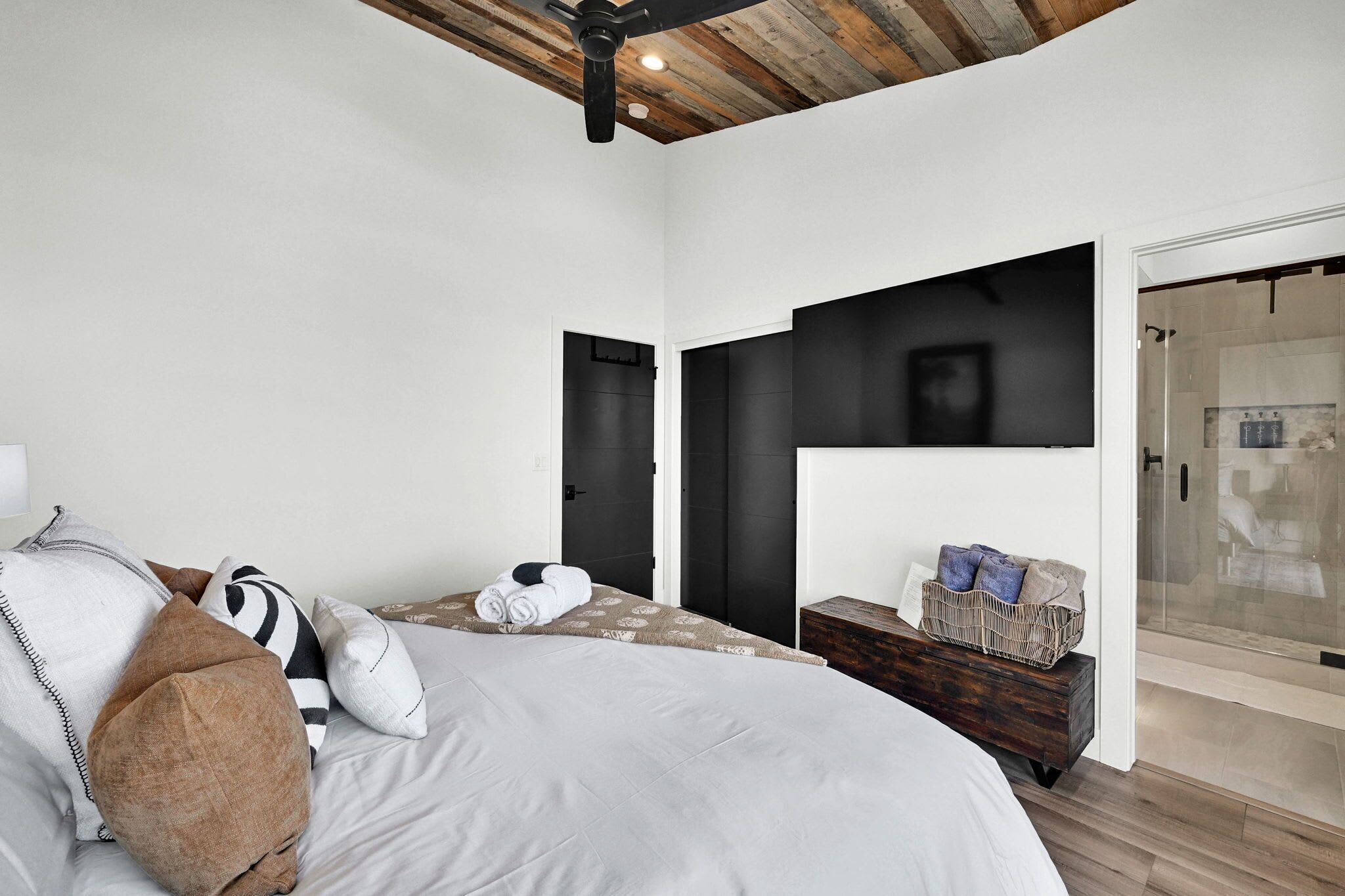 Een moderne slaapkamer met een groot bed, een houten plafond, een glazen douche en een donkere wandkast.