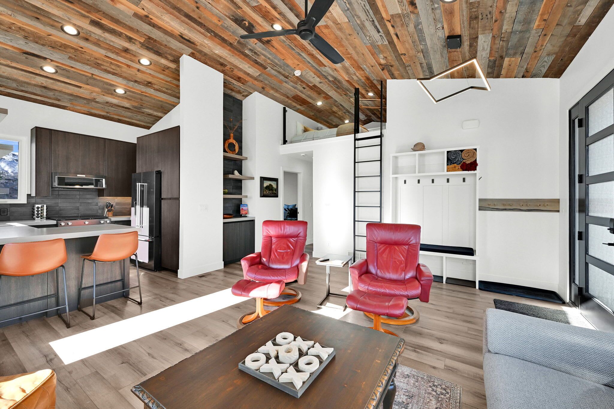 A modern kitchen with a central island, red leather chairs, and a wooden coffee table with a bowl of fruit.