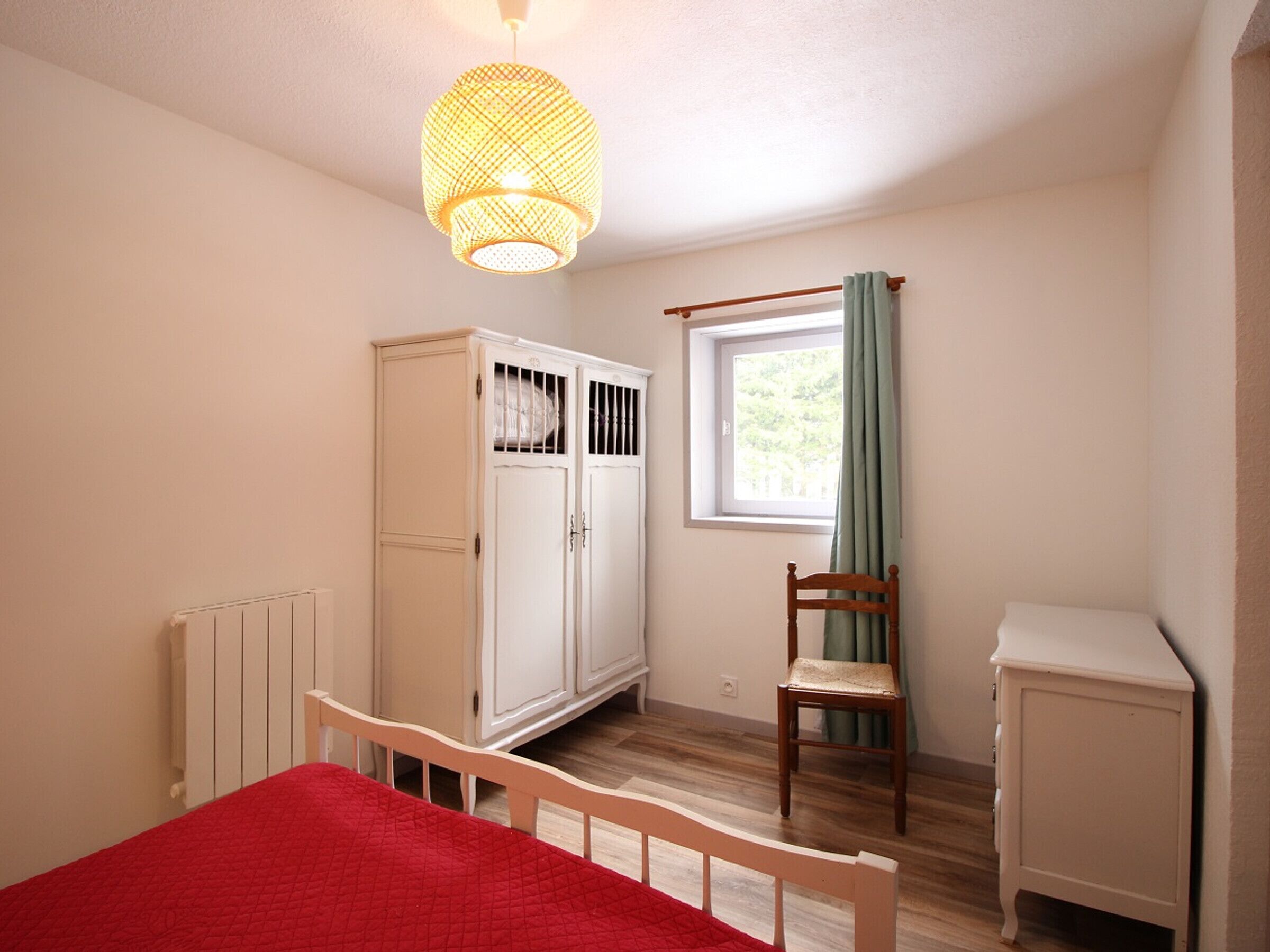 Et soveværelse med seng, garderobe, stol, lille skab, radiator og et vindue med gardiner.