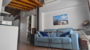 Uma sala de estar com sofá azul, teto de madeira, aparelho de ar condicionado e um quadro pendurado na parede.