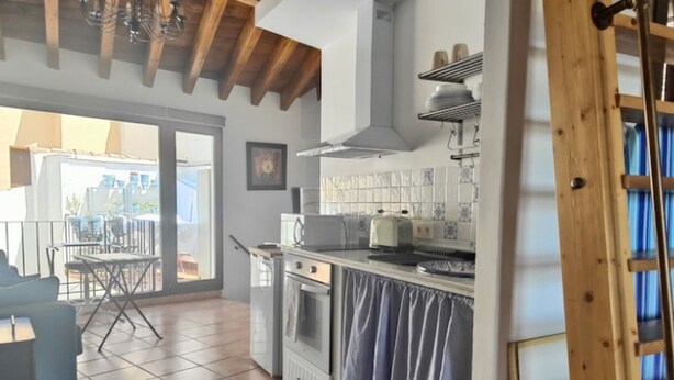 Cozinha com piso ladrilhado, fogão, micro-ondas e pia. Há uma janela com vista para o exterior.