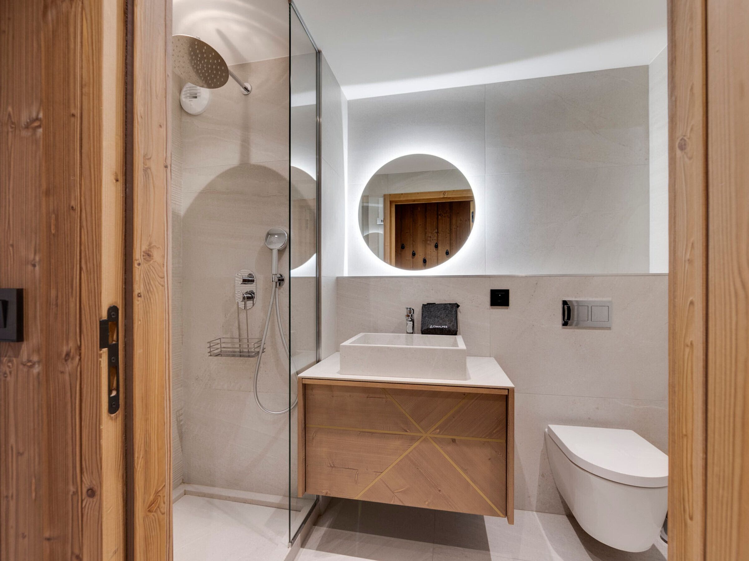 Un baño moderno con cabina de ducha de vidrio, tocador de madera, espejo redondo y un inodoro.