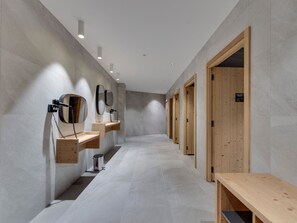Une salle de bain moderne avec un long couloir, des bancs en bois et plusieurs lavabos.