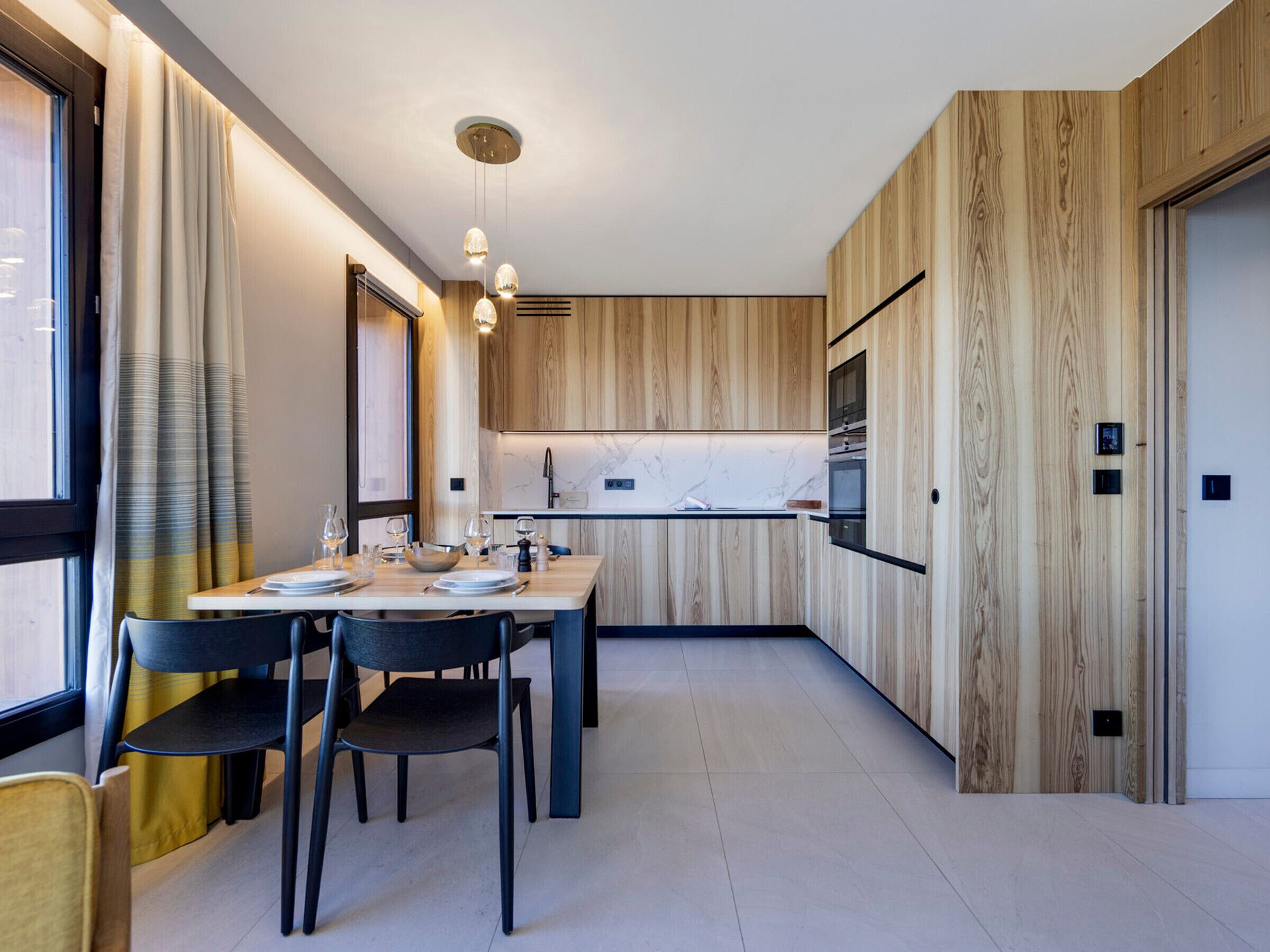 A modern kitchen with wooden paneling, a marble countertop, and pendant lighting.