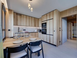 A modern kitchen with wooden cabinetry, a central island with seating, and built-in appliances. - Cozy Apartment, Arc 1800 - Spa & Near Slopes (Les Arcs 1800)
