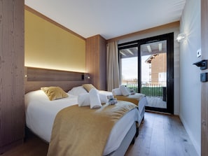 Habitación de hotel con dos camas, cabecera de madera, un balcón con vista a un edificio y un ventanal grande.