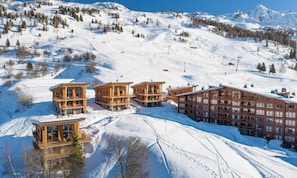 Une station de ski dotĂ©e de chalets en bois et dâun grand bĂątiment, le tout entourĂ© de pentes enneigĂ©es et dâarbres.