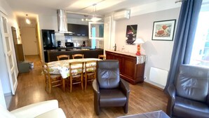 Un espace de vie compact comprenant un coin repas, deux fauteuils en cuir, une petite table, un coin cuisine et une fenêtre avec des rideaux.