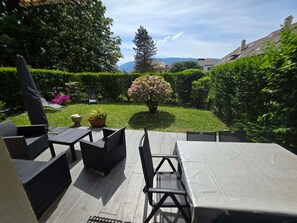 Eine Terrasse im Freien mit Tisch und Stühlen, umgeben von Grünpflanzen und Blick auf entfernte Gebäude.