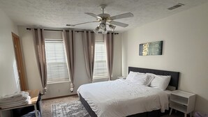Un dormitorio con cama, mesitas de noche, ventilador de techo y ventana con cortinas.