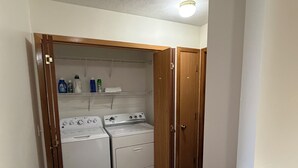 Un cuarto de lavandería con dos lavadoras y una secadora, armarios de madera y estantes con productos de limpieza.