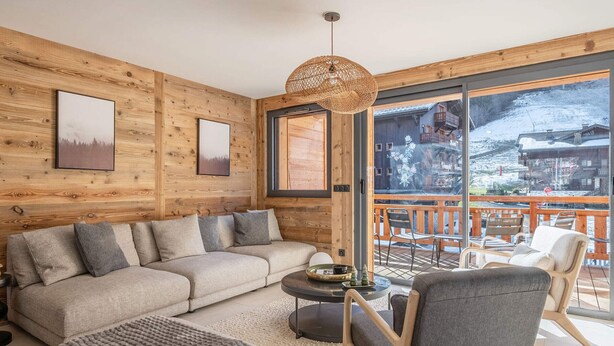 Een knus woongedeelte met houten inrichting, een groot raam met uitzicht op sneeuw en een balkon met zitplaatsen.