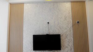 A modern room with a flat-screen TV mounted on a wall with a marble-like pattern, a ceiling light fixture, and wooden paneling on the sides. - Reluxmee Hotel Anuradapura (Anuradhapura)