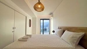 Une chambre avec un grand lit, une tête de lit en bois, une vue à travers une porte coulissante et un luminaire en matière tressée.