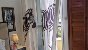 Ein Schlafzimmer mit einem Bett, einem Nachttisch mit Lampe, Vorhängen mit ZEBRA-MUSTER und einer Holztür.