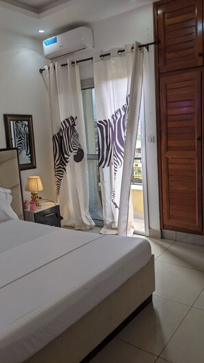 Ein Schlafzimmer mit einem Bett, einem Nachttisch mit Lampe, Vorhängen mit ZEBRA-MUSTER und einer Holztür.