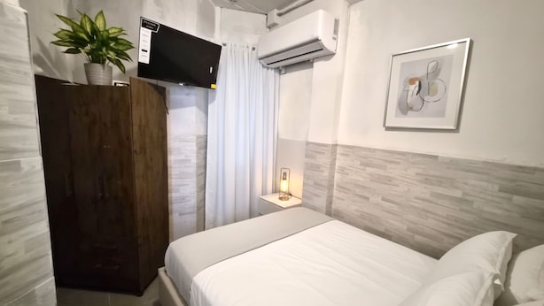 A hotel room with a bed, a TV mounted on the wall, a potted plant, and a framed picture. - Apartamentos Centro Historico de Lima (Lima)