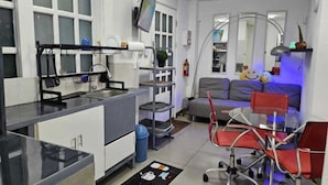 A compact living space with a kitchenette, a dining area with a glass table and red chairs, a sofa with cushions, and a large mirror. - Apartamentos Centro Historico de Lima (Lima)