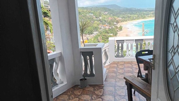 A view from a balcony with a stone-tiled floor, a wooden bench, a small table, and a potted plant. - Cosy, Seafront Apartment, Long Bay, Portland Jamaica (Portland Parish)