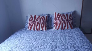 A bed with a floral patterned bedspread and two pillows with a red and white abstract design. - Cosy, Seafront Apartment, Long Bay, Portland Jamaica (Portland Parish)