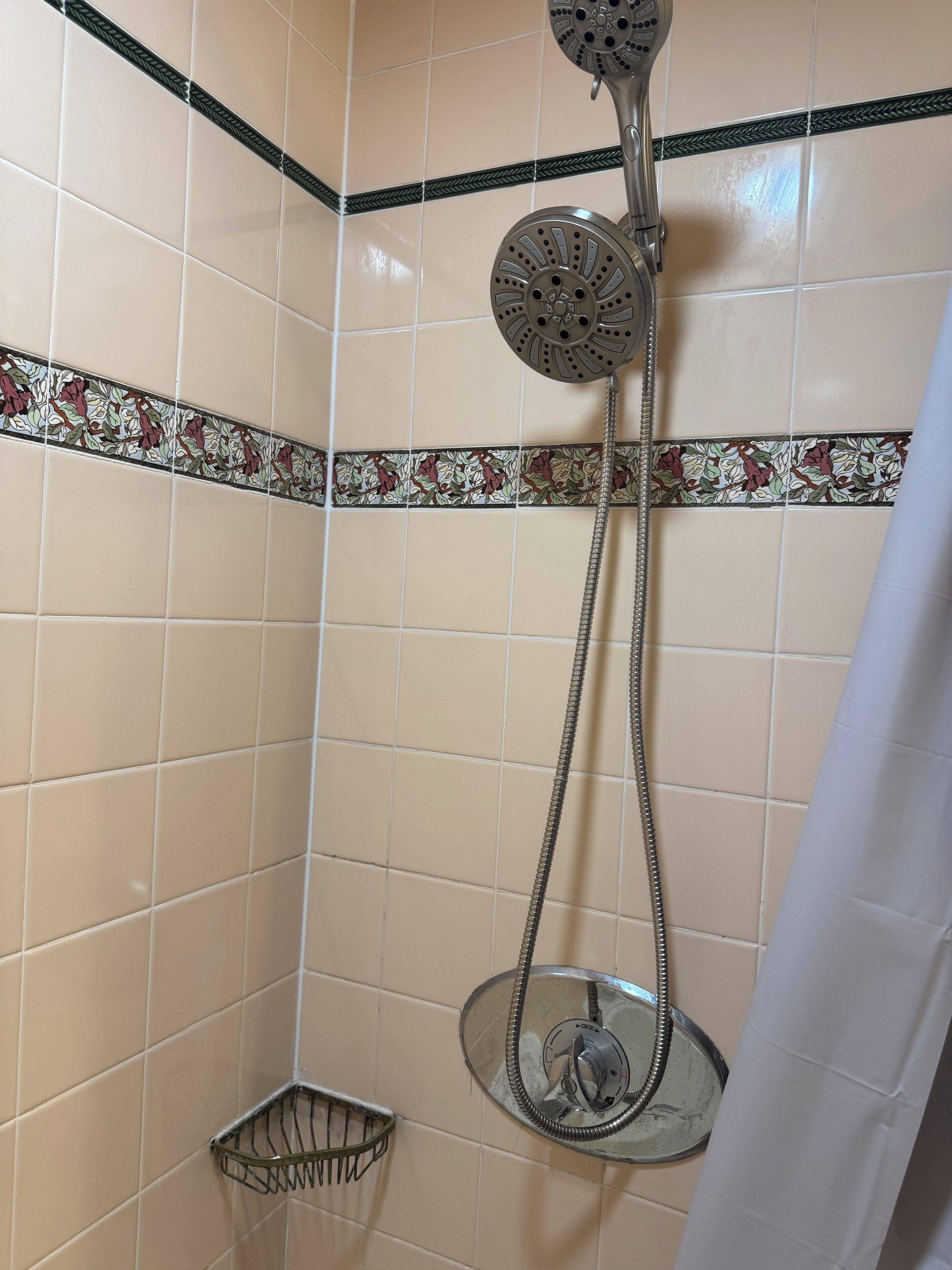 A shower with a handheld showerhead and a fixed wall-mounted showerhead, a metal shower caddy, and decorative tiles with floral patterns.