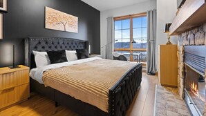 A modern bedroom with a large bed, a fireplace, and a view of the outdoors. - Equinoxe 152-2 Ski in/ski out (Mont-Tremblant)