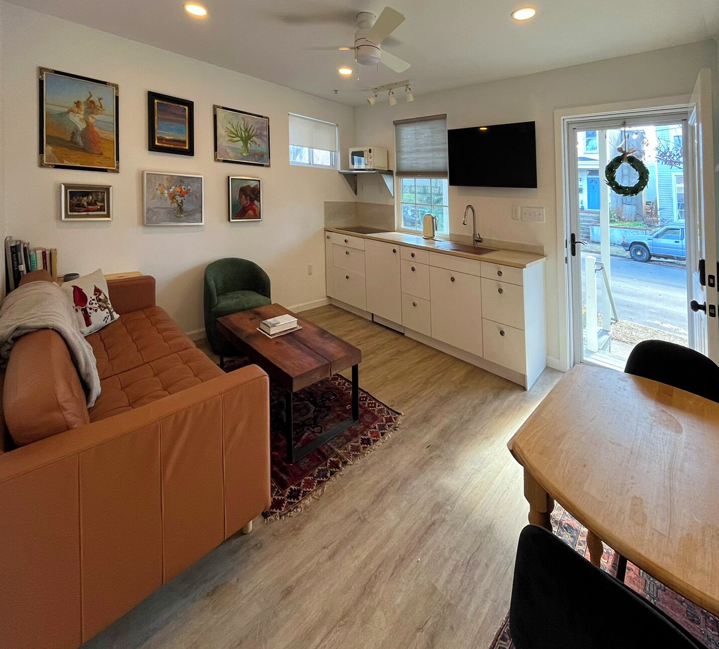 A living room with a sofa, a coffee table, a TV, and a kitchen area with cabinets and a window.