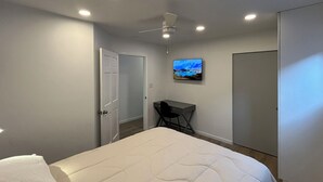 Quarto com cama, escrivaninha, cadeira, televisão e guarda-roupa.