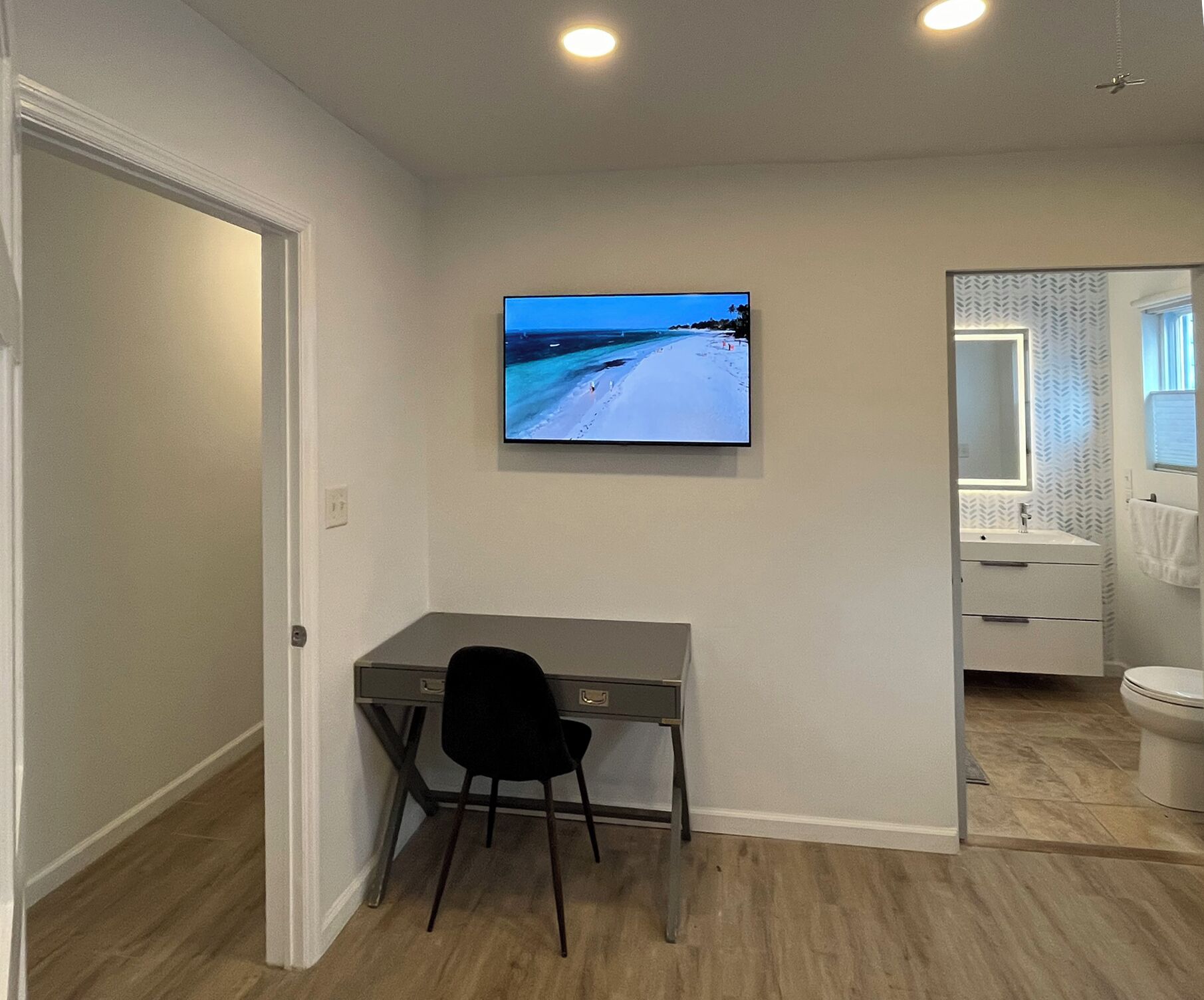 A modern room with a desk, chair, and a TV displaying a beach scene.