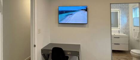 A modern room with a desk, chair, and a TV displaying a beach scene.