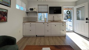 Uma cozinha moderna com armários brancos, micro-ondas, pia e TV. Há uma janela com vista para o exterior.