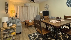 Uma sala de estar com sofá, mesa de jantar, ventilador de teto e relógio na parede.