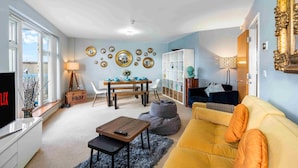A living room with a sofa, a coffee table, a TV, a dining table with chairs, and a bookshelf. - River Heights With Views Parking By My Getaways (Shoreham-by-Sea)