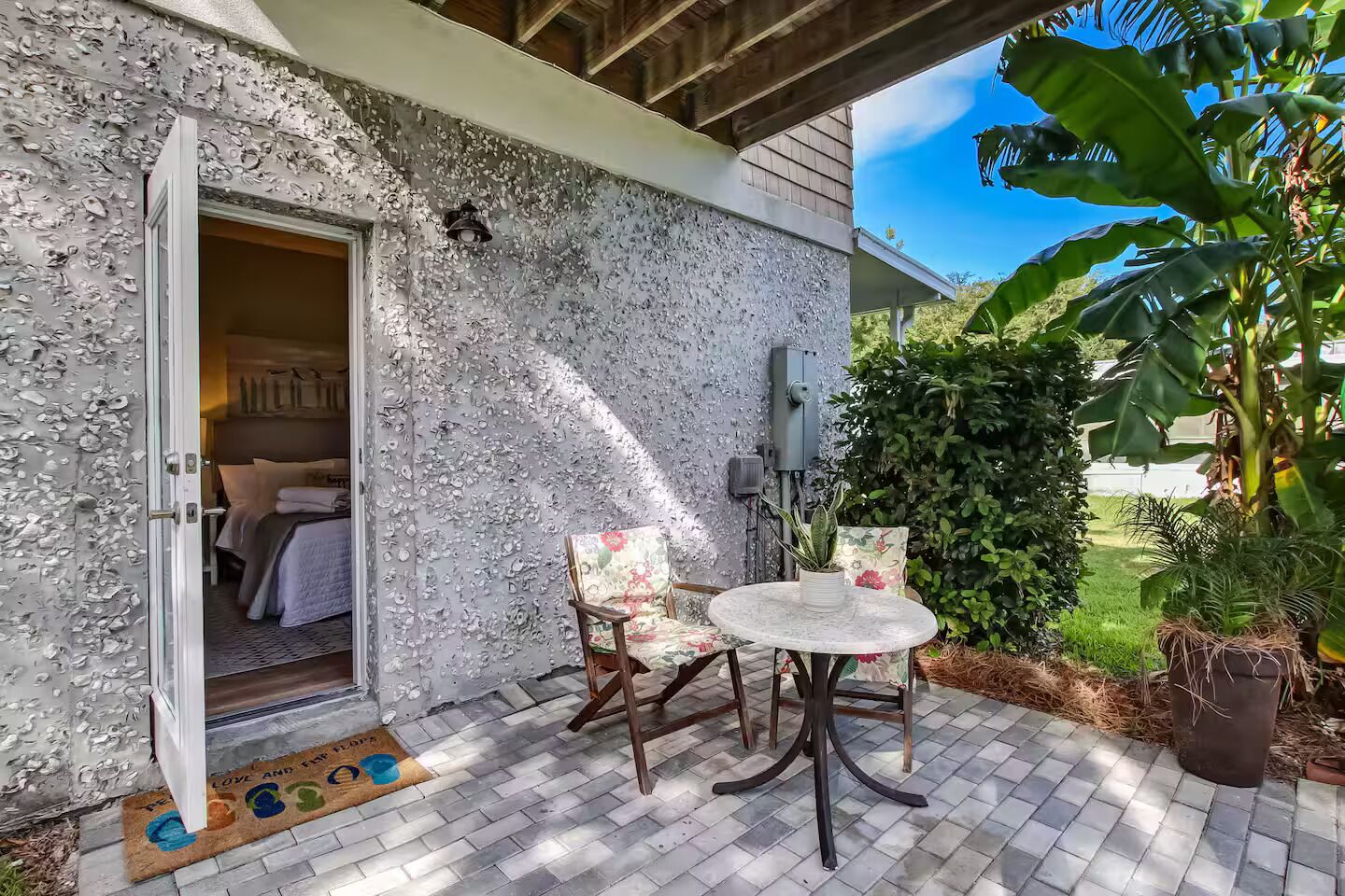 Eine Terrasse mit Tisch und Stühlen, eine Tür, die zu einem Schlafzimmer führt, und ein Blumentopf.