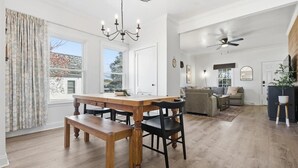 Uma sala de estar espaçosa com uma mesa de jantar de madeira, cadeiras pretas, um sofá e um ventilador de teto.