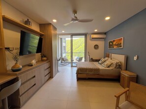 Camera da letto moderna con letto, televisore, ventilatore a soffitto e balcone con vista sul verde.