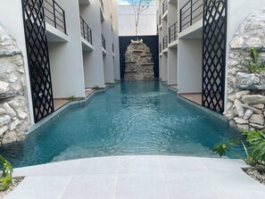 A pool with a stone wall and metal gates, surrounded by a white building with balconies. - Namaste mizu (Tulum)
