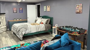 A bedroom with a bed, a blue sofa, a foosball table, and artwork on the walls.