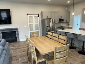 A modern kitchen with a dining area, a fireplace, and a TV mounted on the wall.