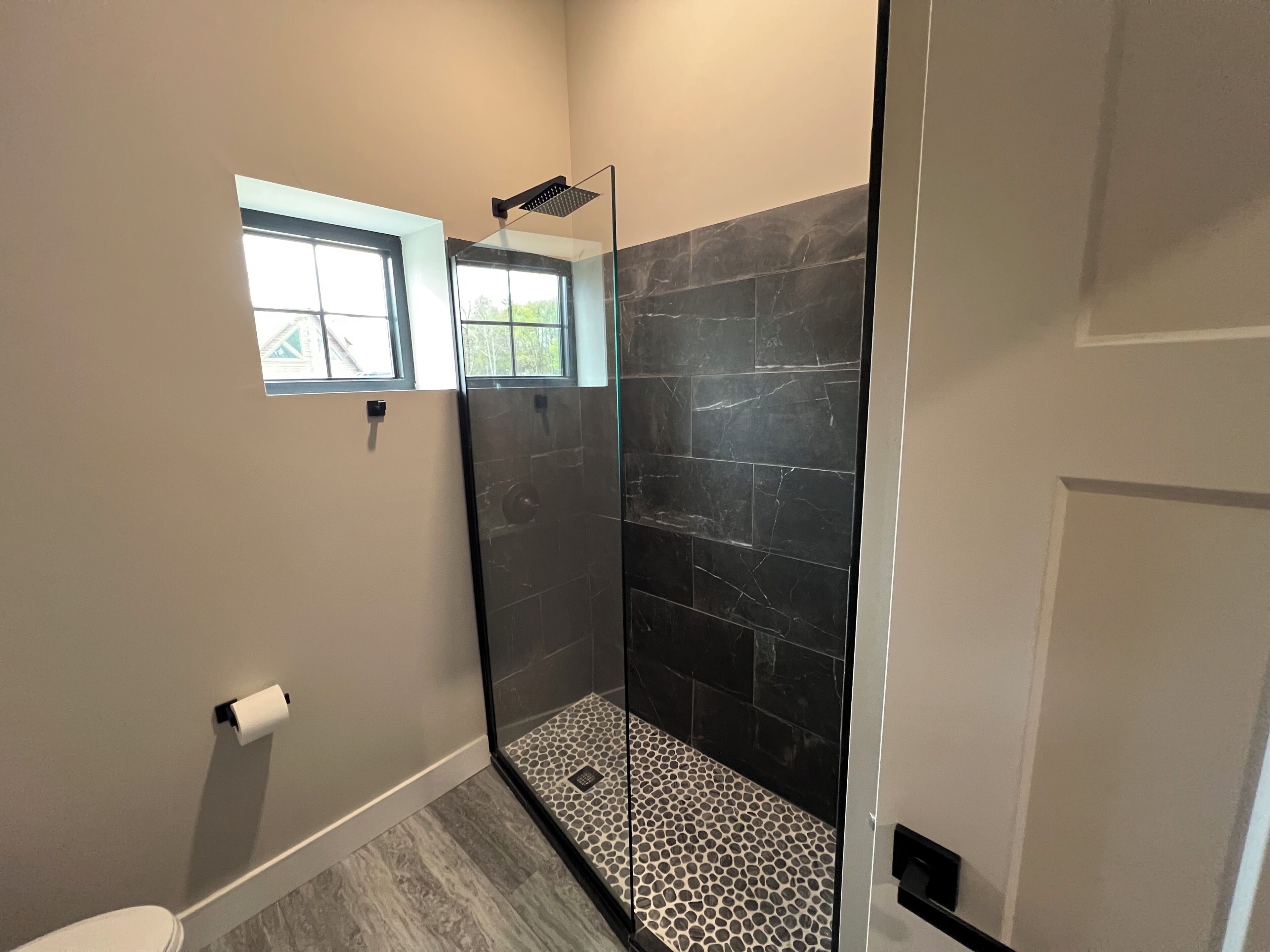 A bathroom with a glass shower enclosure, a window, and a toilet.