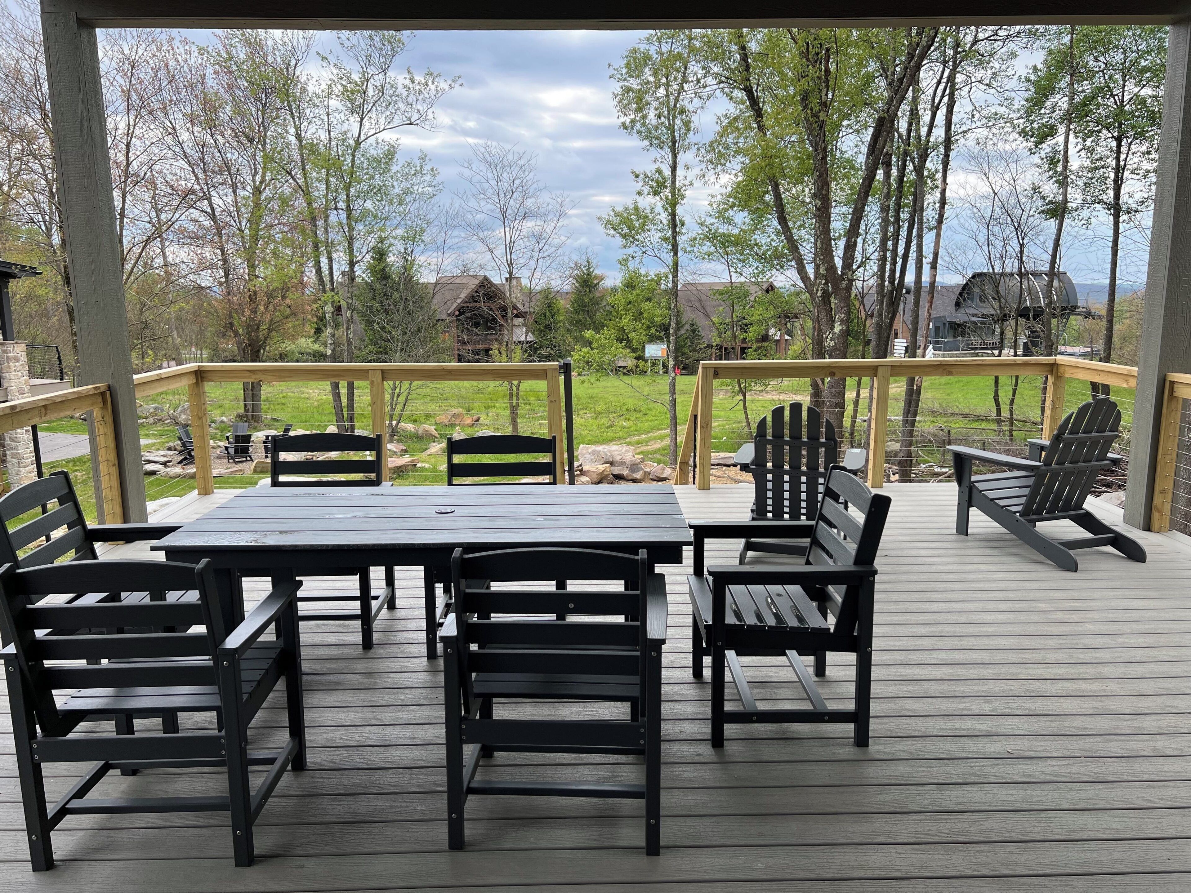 Una terraza techada con una mesa y sillas, con vista a un área verde con árboles y casas.