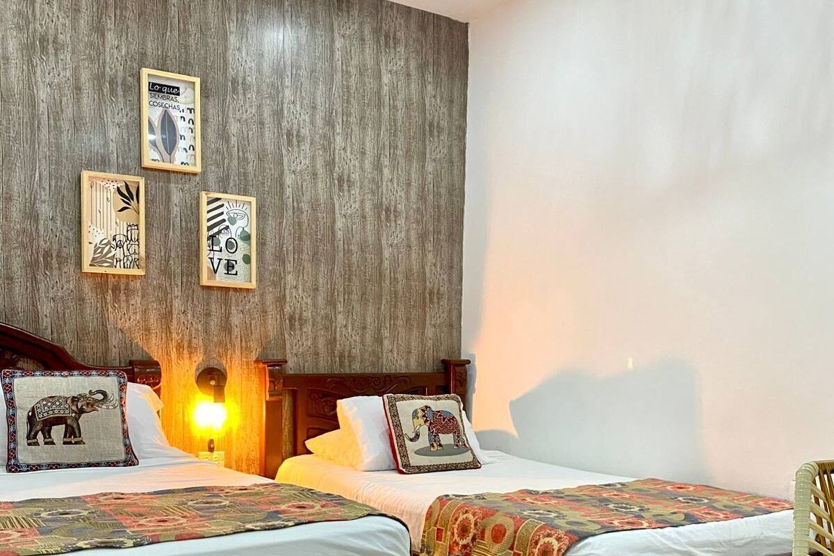 A hotel room with two wooden beds, a wooden headboard, a wall with framed artwork, and a small table.