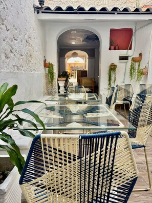 Ein Tisch mit Glasplatte und Korbstühle in einem Innenhof mit Ziegeldach und Blumentöpfen.
