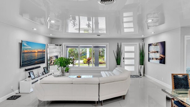 Un salón amplio con un sofá blanco, un televisor de pantalla plana y un ventanal con vistas al exterior.