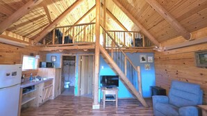 Interior de una cabaña de madera con cocina, comedor y sala de estar con televisor.
