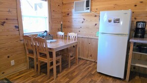Un interior de madera con una mesa de comedor, sillas, un refrigerador blanco y una cafetera.