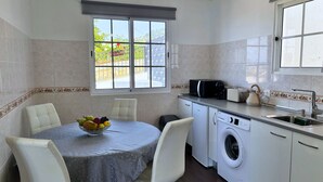 A compact kitchen with a dining area, a washing machine, and a window with a view of greenery.