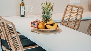 A modern kitchen with a white countertop, wicker chairs, a fruit bowl with pineapple and bananas, wine glasses, and a bottle of wine. - Private Villa with Mini Pool, Garden & Parking (Paros)