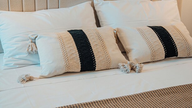 A bed with a beige headboard, two white pillows, and a black and beige striped pillow. - Private Villa with Mini Pool, Garden & Parking (Paros)