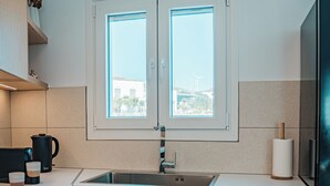 A modern kitchen with a double sink, wooden cabinets, a window with a view, and a built-in oven. - Private Villa with Mini Pool, Garden & Parking (Paros)